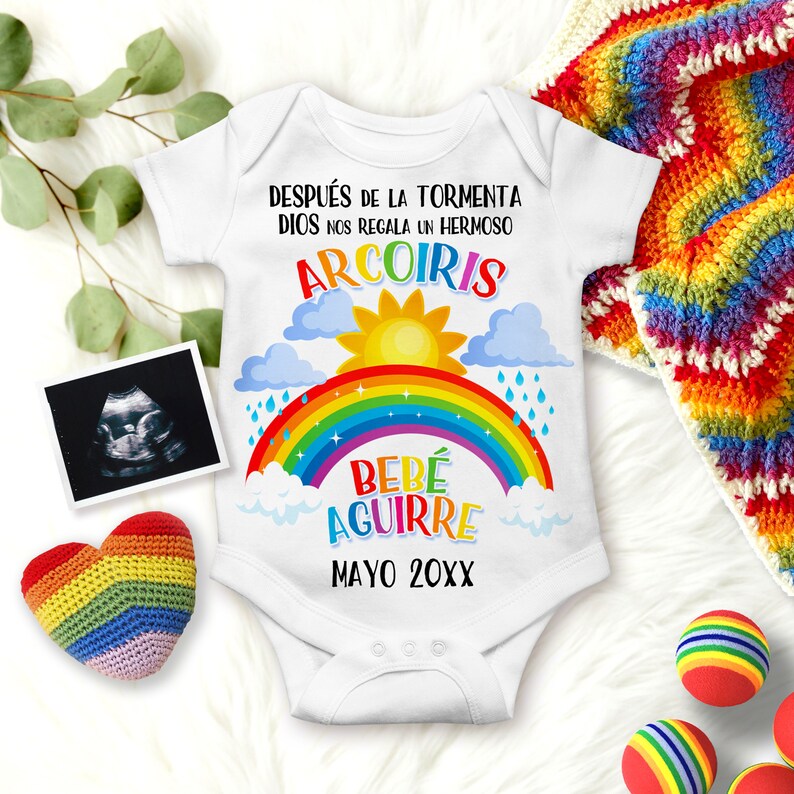 May include: White baby onesie with a rainbow, clouds, sun, and raindrops. The text reads "DESPU&Eacute;S DE LA TORMENTA DIOS NOS REGALA UN HERMOSO ARCOIRIS BEB&Eacute; AGUIRRE MAYO 20XX".