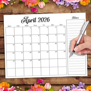 Puede incluir: Un calendario blanco para abril de 2026 con un diseño de cuadrícula, que muestra los días de la semana y las fechas. El calendario está sobre una superficie de madera, rodeado de flores coloridas. Una mano con un bolígrafo plateado escribe en el calendario.