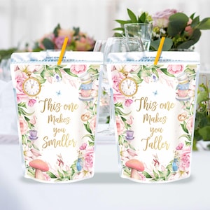 Puede incluir: Dos bolsas blancas con un tema caprichoso de Alicia en el País de las Maravillas. Las bolsas presentan un diseño floral con tazas de té, relojes y hongos. Una bolsa dice "Esta te hace más pequeño" y la otra dice "Esta te hace más alto".