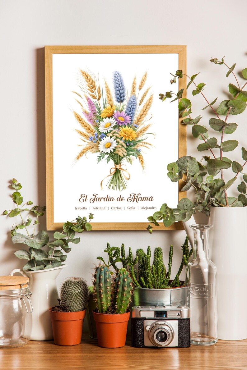 May include: A framed print with a watercolor illustration of a floral bouquet, including wheat, daisies, and lavender. The text "El Jardin de Mama" is displayed, with names below. The print is in a wooden frame, surrounded by plants.