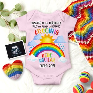 May include: Pink baby onesie with a rainbow, clouds, sun, and raindrops. The onesie says "DESPU&Eacute;S DE LA TORMENTA DIOS NOS REGALA UN HERMOSO ARCOIRIS BEBE AGUILAR ENERO 2021".