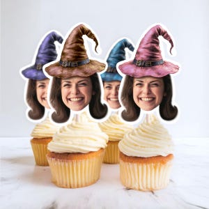 Puede incluir: Cupcakes cubiertos con caras sonrientes que llevan sombreros de bruja morados, marrones, azules y rosas. Los cupcakes tienen bizcocho amarillo y glaseado blanco. Un capricho divertido y festivo para una fiesta o celebración.