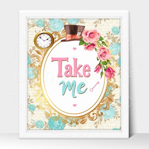 May include: A white framed print with a gold oval frame and a white background. The frame is decorated with blue and gold floral designs. Inside the frame is a pink and blue sign that says "Take Me" with a small gold key to the right of the text. A top hat with a red and white band is above the sign.