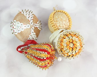 May include: Four vintage Christmas ornaments decorated with sequins and beads. The ornaments are gold, white, red, and orange.
