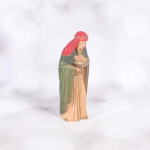 May include: A wooden figurine of a wise man, one of the three kings, wearing a red and green robe and holding a golden cup.