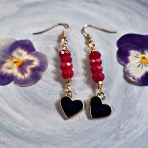 May include: A pair of gold earrings with red gemstone beads and black heart-shaped charms.