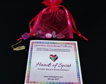 May include: A pink satin pouch filled with pink and purple gemstones. The pouch is tied with a pink ribbon. A small card with the text "Gemstone Enrichment Collection" and "Hands of Spirit" is next to the pouch.
