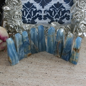 May include: A collection of ten blue and white banded agate crystal points arranged in a semi-circle on a light brown wooden surface.