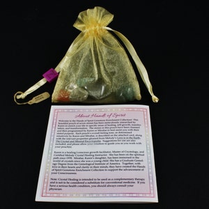 May include: A small pouch of seven gemstones in a gold organza bag with a tag that reads "Hands of Spirit". The pouch is on a white card with the text "About Hands of Spirit" and information about the gemstones and their uses.