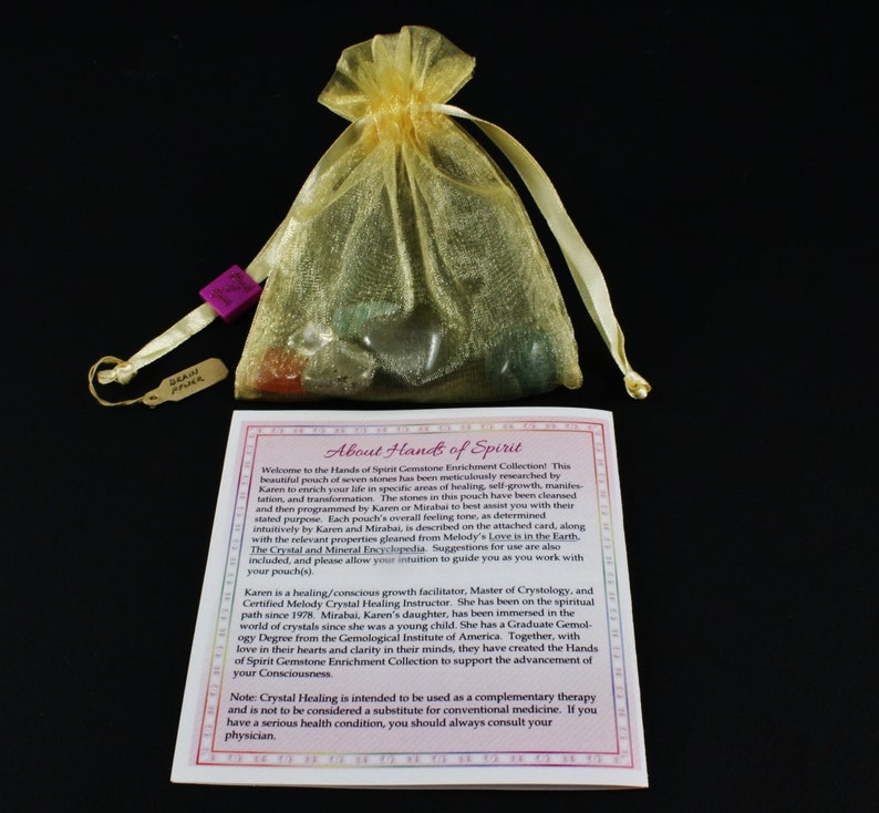 May include: A small pouch of seven gemstones in a gold organza bag with a tag that reads "Hands of Spirit". The pouch is on a white card with the text "About Hands of Spirit" and information about the gemstones and their uses.