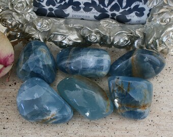 May include: Six tumbled blue calcite stones with brown veins. The stones are smooth and polished, and they have a natural, organic look.
