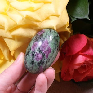 以下が含まれることがあります： 滑らかな楕円形の緑とピンクの宝石。石は黄色と赤のバラの背景に手の中で持たれています。