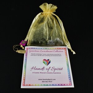 Puede incluir: Una bolsa de organza amarilla llena de piedras preciosas, una pequeña etiqueta con las palabras "Gemstone Plus" y una tarjeta impresa con el texto "Gemstone Enrichment Collection", "Hands of Spirit", "A Crystal, Mineral & Jewelry Experience", "www.handsofspirit.com" y "303-541-9727".