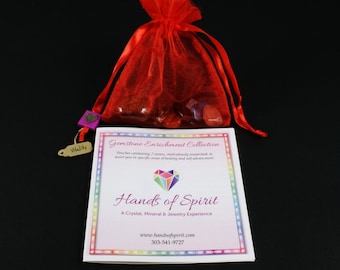 May include: A red drawstring bag filled with small, colorful gemstones. The bag is sitting on a white card with the text "Gemstone Enrichment Collection" and "Hands of Spirit" in black text. The card also includes the website address "www.handsofspirit.com" and the phone number "303-541-9727".