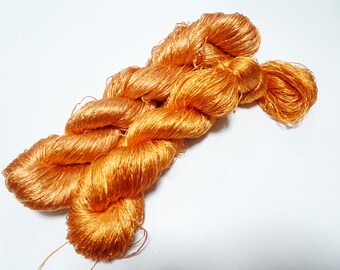 Könnte beinhalten: Ein Knäuel orangefarbener Seide. Der Faden ist weich und glänzend und eignet sich perfekt zum Sticken, Stricken oder Häkeln.