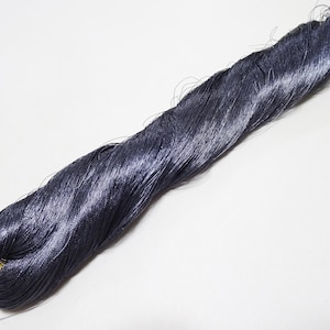 Può includere: Un lungo filo metallico grigio scuro, attorcigliato e raggruppato. Il filo è lucido e ha un leggero bagliore.