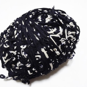 May include: A ball of dark navy blue and white fabric strips. The strips are loosely woven together, creating a textured, irregular surface. The white strips are interspersed throughout the navy blue, creating a contrasting pattern. The fabric appears to be soft and pliable.
