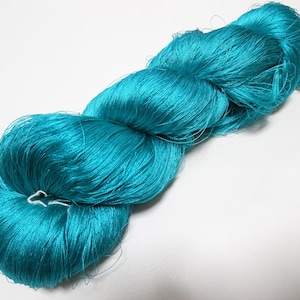 May include: A skein of bright turquoise yarn, tightly wound and textured. The yarn has a solid, saturated colour, with a slight sheen. The fibres are fine and appear soft. The yarn is likely used for knitting or crocheting projects.
