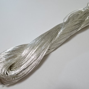 Può includere: Un rocchetto di filo metallico argentato. Il filo è avvolto stretto e ha una finitura lucida e riflettente.