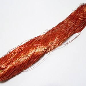 Peut inclure: Une bobine de fil de cuivre de couleur brun rougeâtre avec une finition métallique brillante. Le fil est enroulé serré et semble très fin.