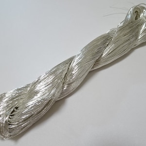 Puede incluir: Una bobina de hilo metálico plateado, ideal para manualidades y la elaboración de joyas.