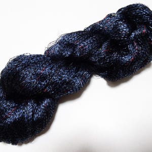 May include: A skein of dark blue yarn with subtle red and green flecks. The yarn appears soft and slightly textured, ideal for knitting or crocheting projects. The yarn is displayed against a white background.