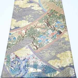 Può includere: Un tessuto ornato con un design paesaggistico dettagliato. Il tessuto presenta un patchwork di motivi, tra cui nuvole, alberi ed elementi floreali in tonalità oro, blu e rosa. Il design complessivo è intricato e visivamente ricco.