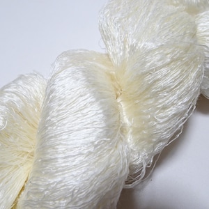 May include: A skein of white silk yarn, with a soft, fluffy texture. The yarn is tightly wound and has a delicate, almost ethereal appearance.