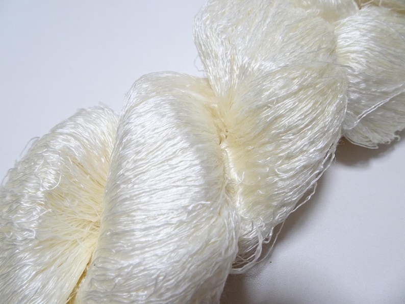 May include: A skein of white silk yarn, with a soft, fluffy texture. The yarn is tightly wound and has a delicate, almost ethereal appearance.