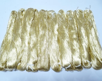 May include: A collection of golden-yellow silk threads, bundled and tied with white string. The threads have a soft, shimmering appearance, suggesting a luxurious textile. The bundles are arranged closely together, filling the frame.