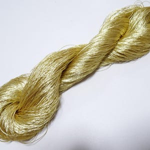 May include: A skein of gold-coloured thread, tightly wound and twisted. The thread has a shiny, metallic appearance, suggesting it may be silk or a similar material. The thread is on a white background.
