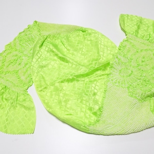 Op de afbeelding: Felgroen neonkleurig stof met een ruitpatroon en gefranjerde randen. De stof heeft een zachte glans en lijkt licht van gewicht. Het ontwerp bevat delen met een gestructureerd, bijna kantachtig patroon. De algehele esthetiek is delicaat en levendig.