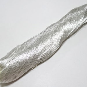 Könnte beinhalten: Eine Spule mit silbernem Metallic-Garn. Das Garn ist fest gewickelt und hat eine glänzende, reflektierende Oberfläche.