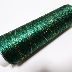 May include: A spool of dark green thread with a metallic sheen and gold accents. The thread is wound around a white core, creating a cylindrical shape. Ideal for sewing, embroidery, or other craft projects.