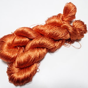 May include: A close-up of a bundle of orange silk thread. The thread is twisted and knotted, creating a textured and intricate pattern.