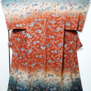 May include: A full-length kimono featuring a gradient color scheme that transitions from a light blue at the top and bottom to a deep orange in the center. The garment is decorated with a repeating pattern of small white flowers and blue birds.