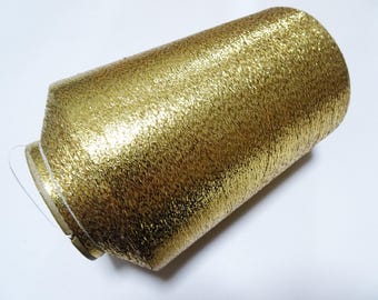 May include: A spool of metallic gold thread, ideal for embroidery or decorative sewing projects. The thread has a textured, shimmering surface, reflecting light. The spool is cylindrical with a white and gold base.
