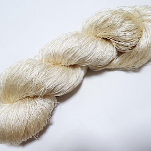 May include: A skein of ivory-colored yarn, tightly twisted into a rope-like form. The yarn appears soft and lustrous, with a slight sheen. The fibers are fine and densely packed, suggesting a high-quality material suitable for various crafting projects.