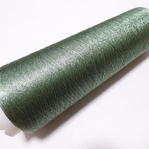 May include: A spool of green thread with a metallic sheen. The thread is tightly wound around a white plastic core. The color is a muted green, with a subtle shimmer. Ideal for sewing, embroidery, or other crafts.