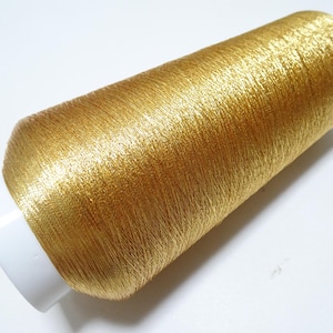 May include: A spool of gold metallic thread. The thread is wound around a white plastic spool.