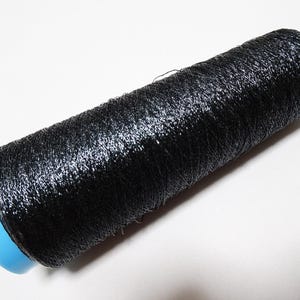 May include: A spool of black thread, tightly wound, with a slight sheen. The thread is wrapped around a light blue plastic core. Ideal for sewing, embroidery, or other crafting projects.