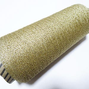May include: A spool of gold metallic thread. The thread is wound around a cardboard spool with a black and white striped label.