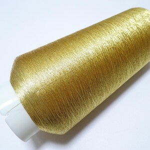 Op de afbeelding: Een spoel goudkleurig metallic garen. De draad is strak gewikkeld rond een witte plastic kern. De draad heeft een glanzende, getextureerde uitstraling en reflecteert licht. Ideaal voor borduren, naaien of andere knutselprojecten.
