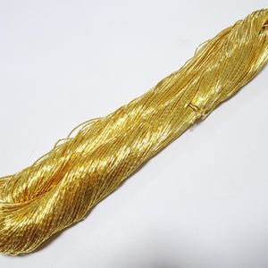May include: A bundle of shiny gold metallic thread, tightly wound and slightly textured. The thread is a bright, solid gold colour, and appears to be made of many fine strands. The bundle is on a white background.