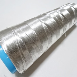 May include: A spool of silver metallic thread wound around a blue plastic bobbin.