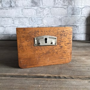 Könnte beinhalten: Eine Holzkiste mit einem Metallverschluss und einem Schlüsselloch. Die Kiste ist braun und hat eine abgenutzte Oberfläche.