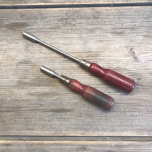 Könnte beinhalten: Zwei vintage Schraubendreher mit Holzgriffen. Die Griffe sind dunkel rotbraun. Die Schraubendreher liegen auf einer Holzoberfläche.