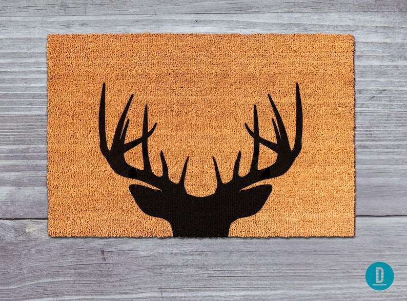 A black silhouette of a deer head with antlers is displayed on a textured orange mat against a wooden background.