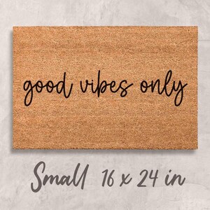 A rectangular, light brown, textured doormat with the text "good vibes only" printed on it.
