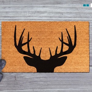 A pair of black boots is positioned next to a wooden surface with a decorative orange mat featuring a black silhouette of a deer's head.